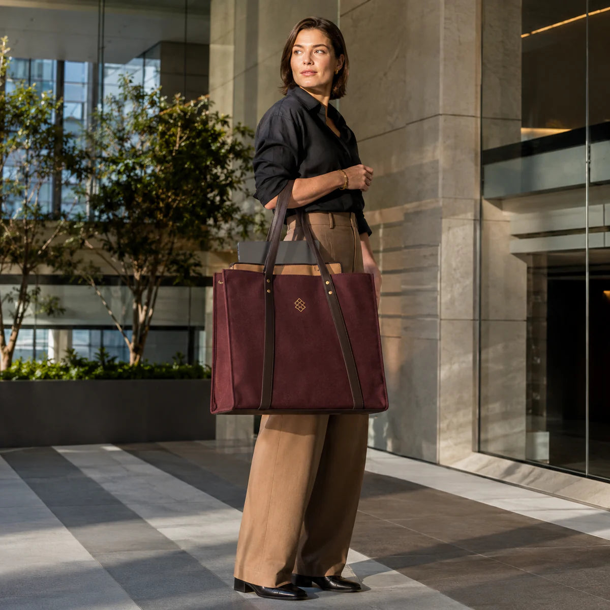 Professional carrying a structured burgundy waxed-canvas gusset tote with leather handles and a subtle gold emblem