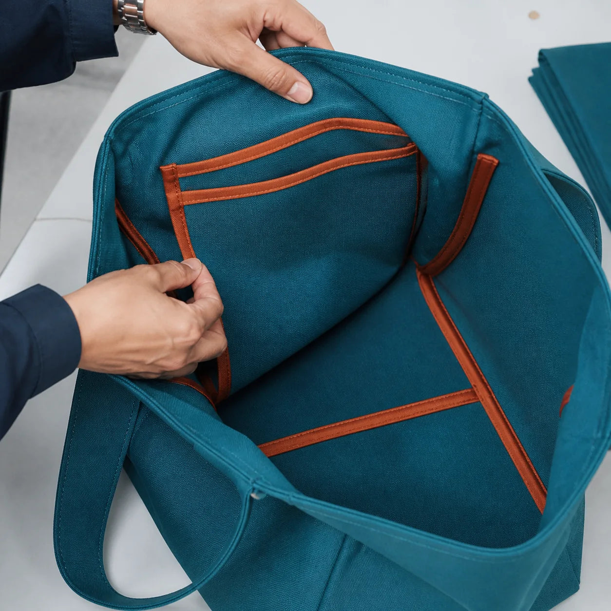 Quality inspector checking clean bound seams and pockets inside a teal canvas tote