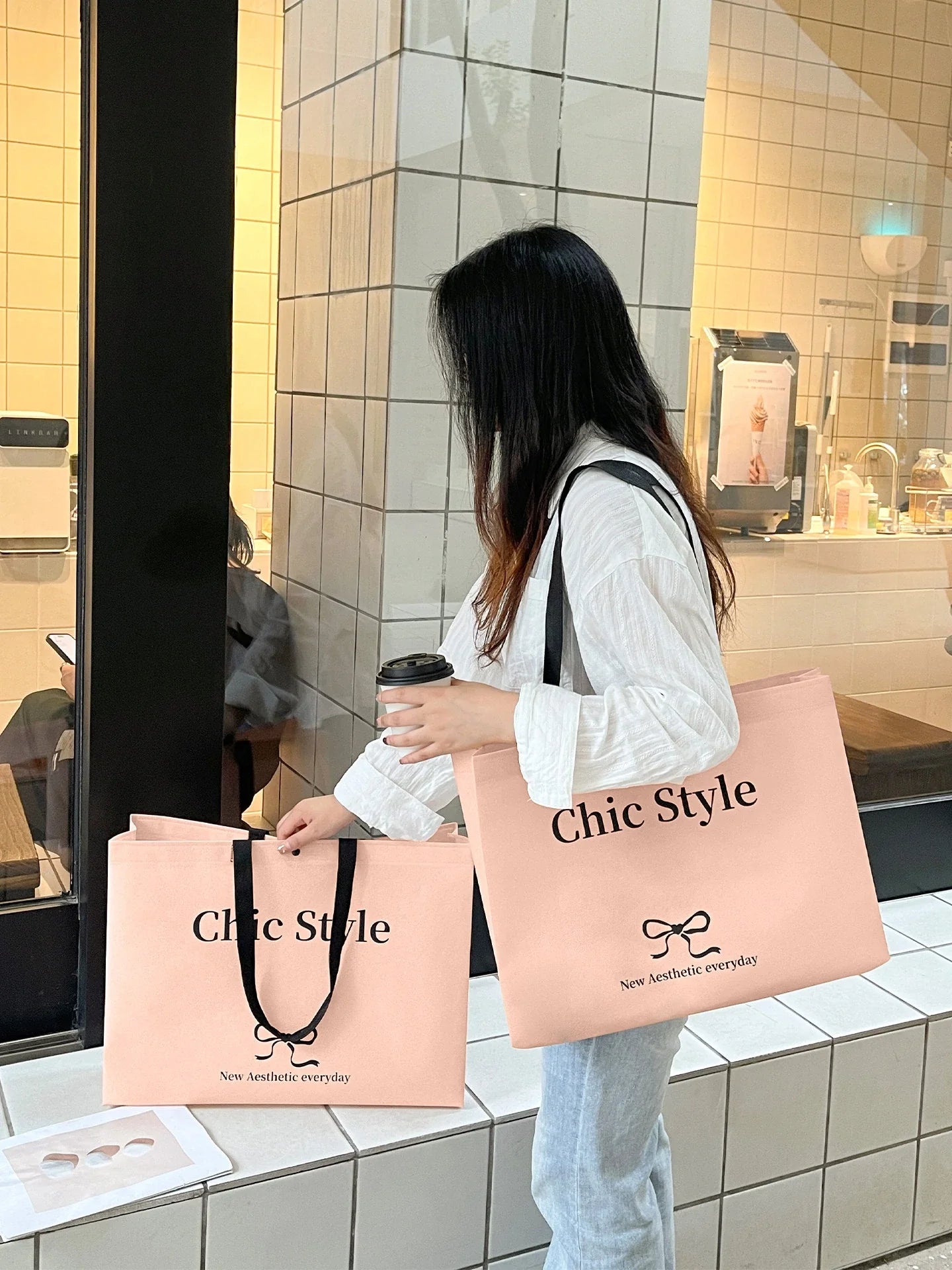 Comprador sosteniendo dos bolsas no tejidas estampadas en rosa claro con asas largas de correas negras