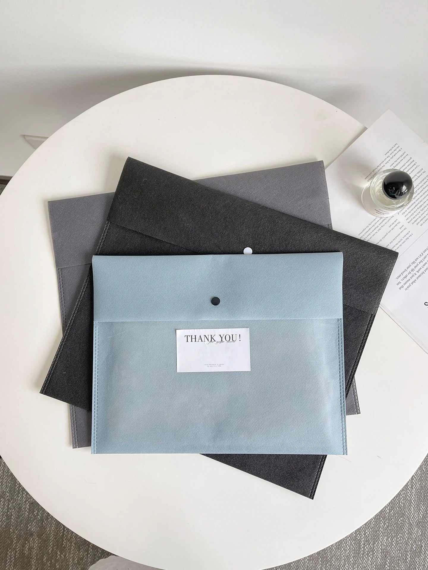 Haze-blue, gray and black non-woven envelope-style bags arranged with visible front snaps