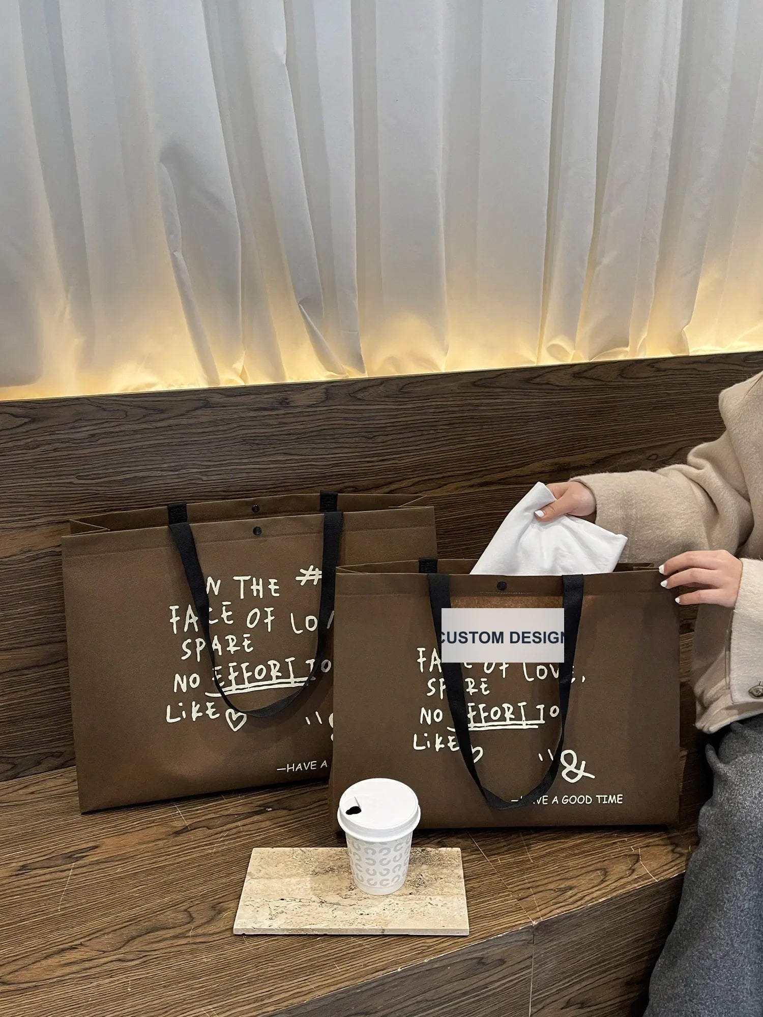 Varias bolsas no tejidas impresas Happy Life marrones con asas de correas negras, con pañuelos blancos colocados en una bolsa