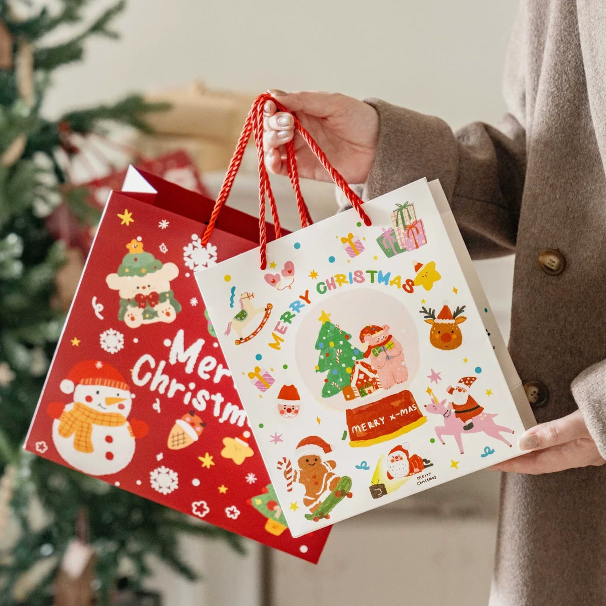 Red and white Christmas gift bags with red rope-style carry handles shown in a holiday setting