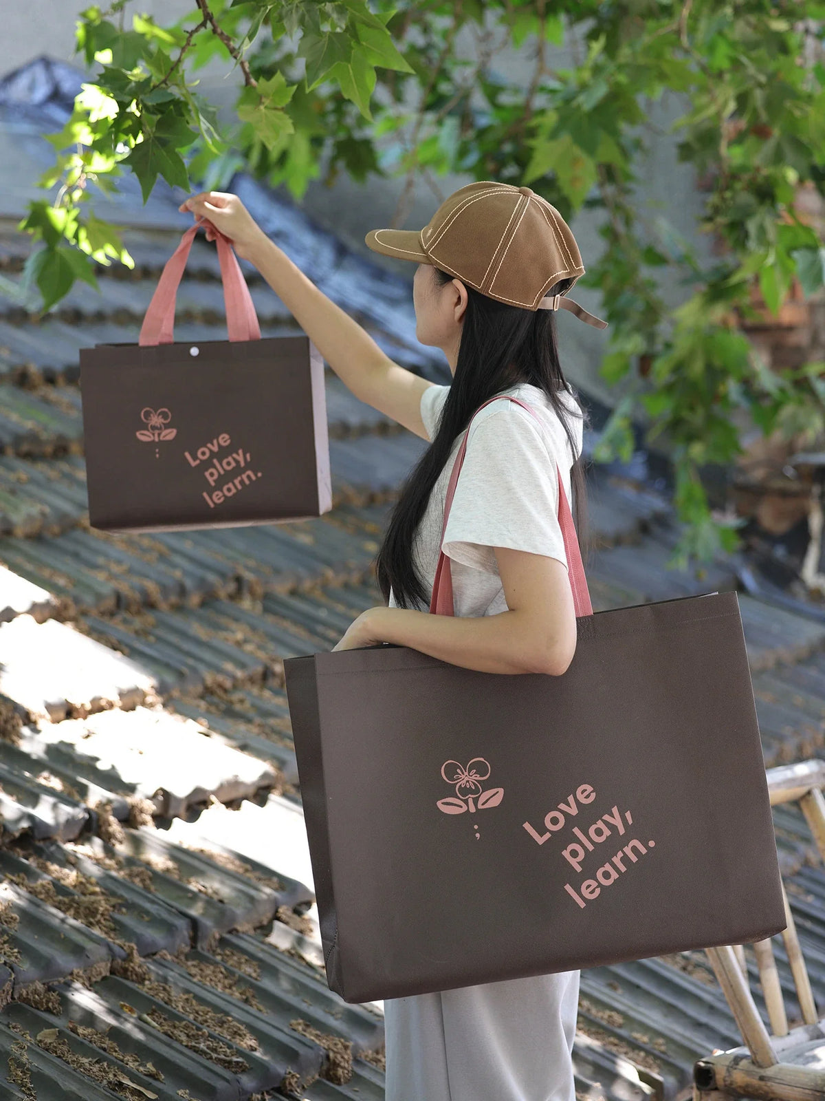 Shopper carrying two brown non-woven totes with pink flat handles in different sizes
