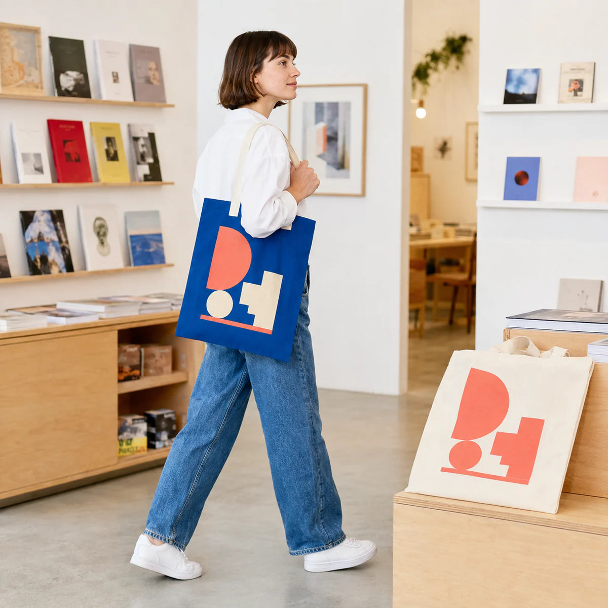 Art-book shop customer carrying a cobalt organic cotton flat tote with a coral geometric screen print