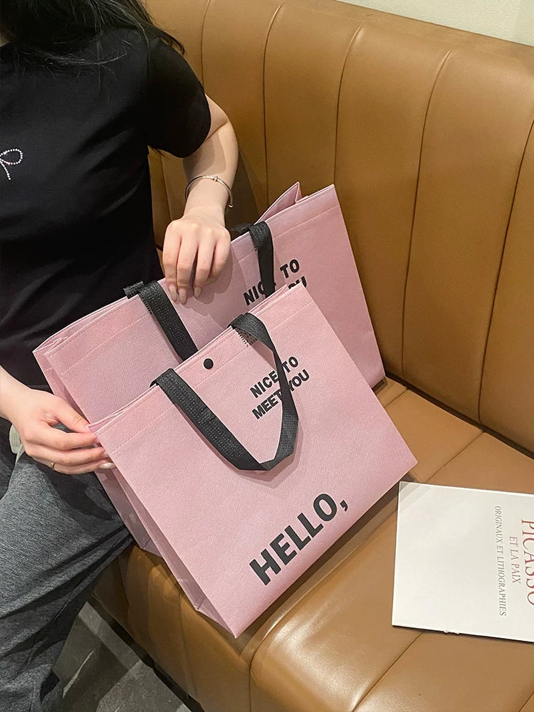 Blush pink non-woven tote bag with black handles in a lifestyle setting