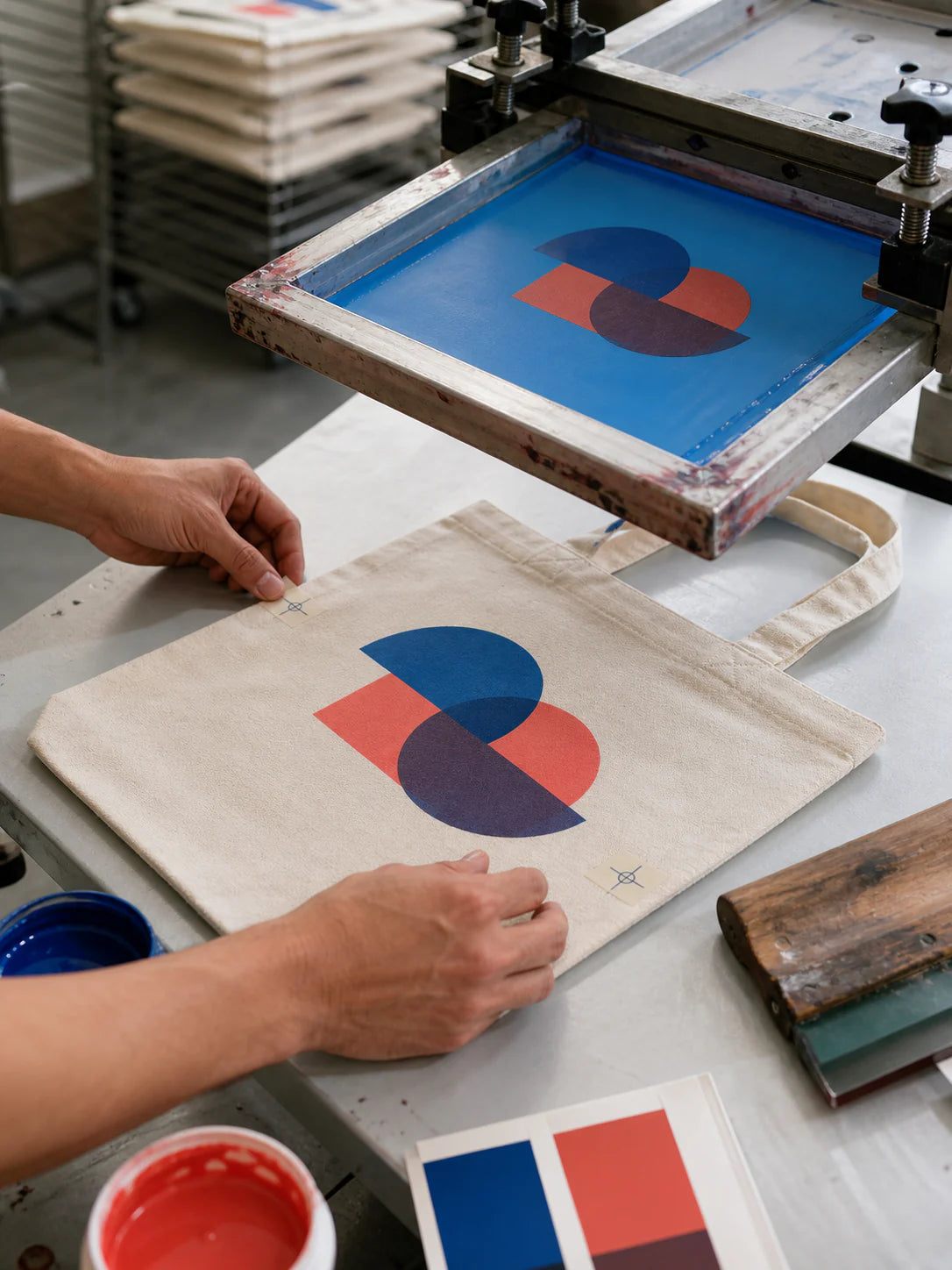 Screen-printing workshop aligning an original two-color geometric mark on a canvas tote