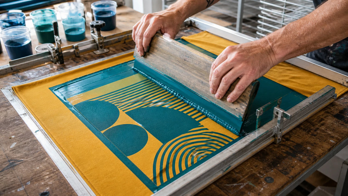 Printer pulling teal water-based ink through a screen onto mustard recycled fabric